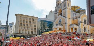 Multidão em frente à Catedral de Florianópolis vê Lula discursar, usando camiseta preta e boné vermelho do MST