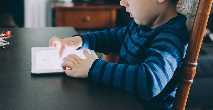 Criança sentada em uma cadeira usa um tablet luminoso em cima de uma mesa