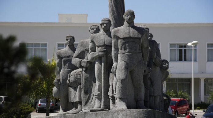 Monumento de pedra cinza em praça retratando imigrantes