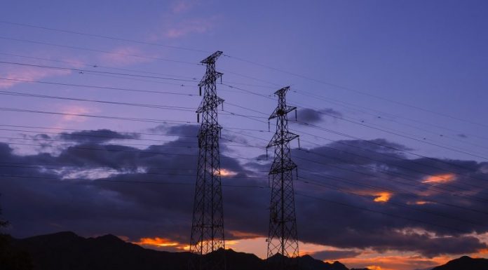 Imagem de duas torres de transmissão de energia elétrica com o por do sol ao fundo