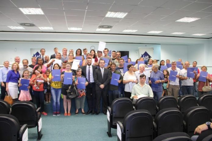 Dezenas de pessoas posam com certificados na frente de um auditório