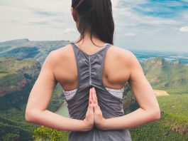 Imagem de uma mulher jovem de costas, com as mãos colocadas para trás em forma de oração; ao fundo, uma paisagem de montanhas