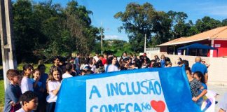 Com uma faixa à frente escrita "a inclusão começa no coração", alunos fazem passeata