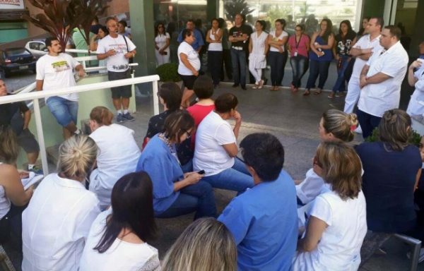 Pessoas sentadas na escadaria em frente ao hospital ouvem um homem falar em pé