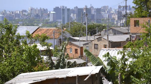 Vista da cidade, com casas pobres em primeiro plano e prédio de classe alta ao fundo