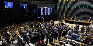 Vista do salão do Senado, com muitas cadeiras e pessoas engravatadas em pé pelo ambiente