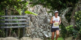 Atleta corre em uma trilha de florianópolis, com um muro de pedra ao fundo e placas de direções ao lado