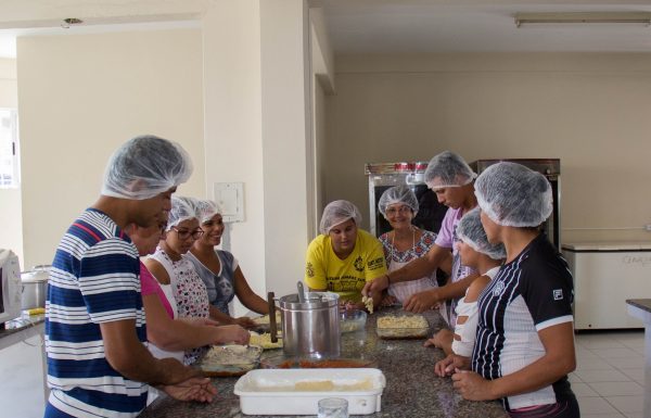 Pessoas usando toucas de higiene sanitária em volta de uma bancada analisam alimentos