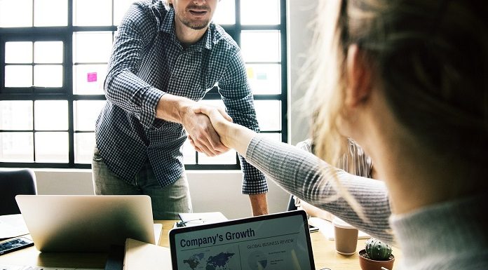 um homem e uma mulher se cumprimentam sobre com as mãos sobre uma mesa de reuniões