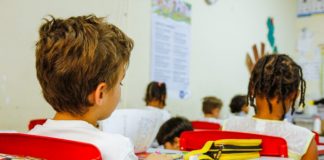 crianças sentadas em carteiras na sala de aula, vista de costas