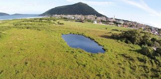 vista aérea de um campo verde com uma pequena lagoa no meio. morro e praia ao fundo