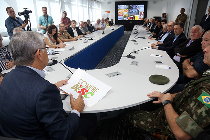 florianopolis_-_reuniao_entre_o_governador_e_setores_podutivos grande mesa de reunião em U com o governador sentado na ponta e visto de costas falando para duas dezenas de pessoas sentadas