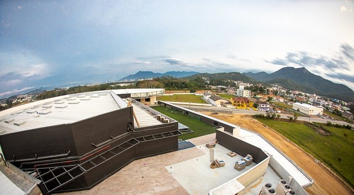 vista aérea de parte do prédio, mostrando um terraço e terreno em baixo, com casas ao fundo da imagem