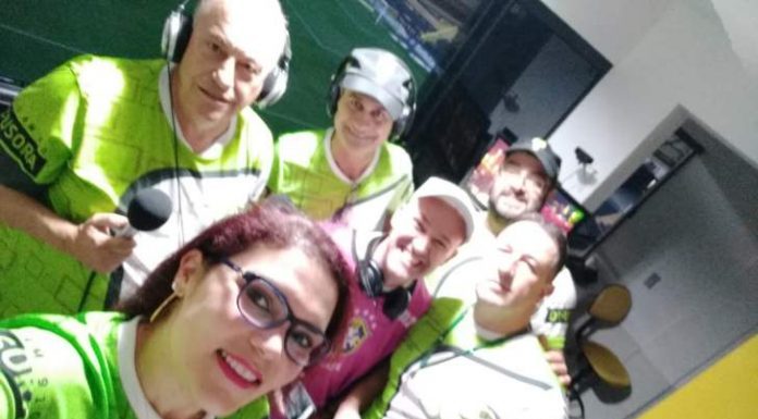 michelle faz selfie com colegas em cabine de transmissão, todos usando o mesmo uniforme verde