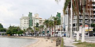 pequena praia onde há calçada alta, ao lado de rua e prédios ao fundo