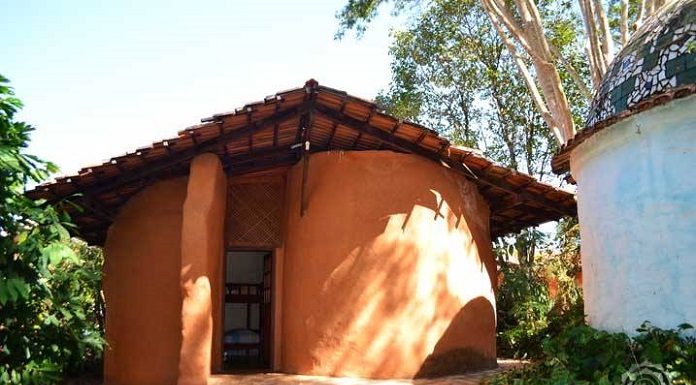 casa com formatos curvos, de cor alaranjada, com algumas plantas em volta