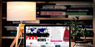 notebook em cima de uma mesa com objetos onde se lê na tela "fake news"