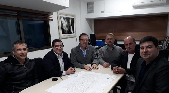 cinco homens reunidos em volta de uma mesa sorriem para foto