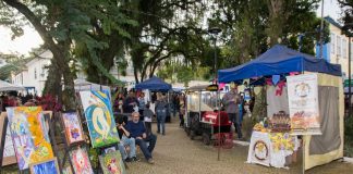 barracas de feiras com diversos produtos expostos; na esquerda, quadros