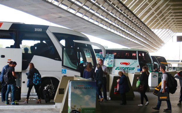 ônibus estacionados em rodoviária, com passageiros circulando na frente