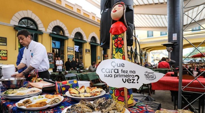 pratos de ostras sobre uma mesa no mercado público com um homem ao lado; há uma placa que diz "que cara fez na sua primeira vez?"