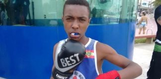 garoto usando protetor de boca e luvas de boxe posa para foto com uniforme fazendo gesto de defesa