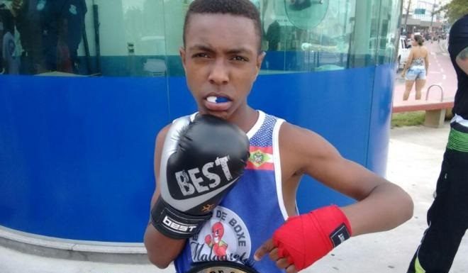 garoto usando protetor de boca e luvas de boxe posa para foto com uniforme fazendo gesto de defesa