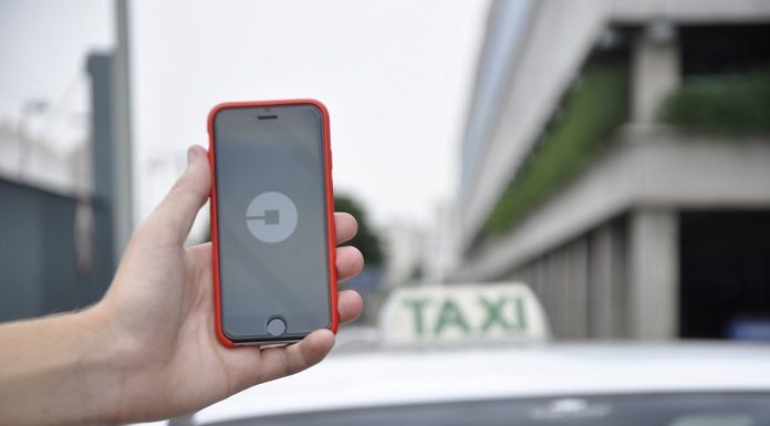 uma mão segurando um celular com o símbolo da uber e atrás um carro com a placa de taxi sobre o teto