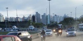 pista em curva cheia de serragem com alguns carros passando e caminhão tombado ao fundo