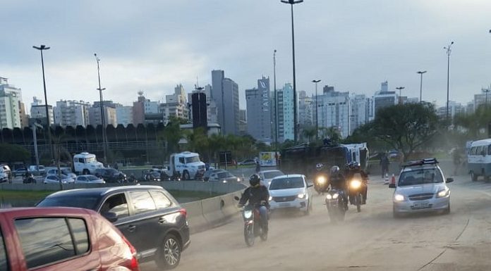 pista em curva cheia de serragem com alguns carros passando e caminhão tombado ao fundo