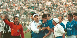 foto do clássico; margarida, de bigode e uniforme vermelho, gesticula com o braço, enquanto membros da equipe técnica do avaí seguram um jogador revoltado