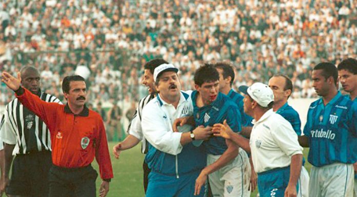 foto do clássico; margarida, de bigode e uniforme vermelho, gesticula com o braço, enquanto membros da equipe técnica do avaí seguram um jogador revoltado