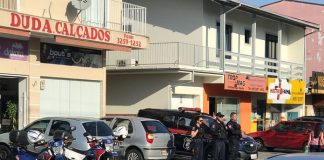 três agentes da guarda parados lado a lado na calçada em frente aos comércios observando o movimento da rua