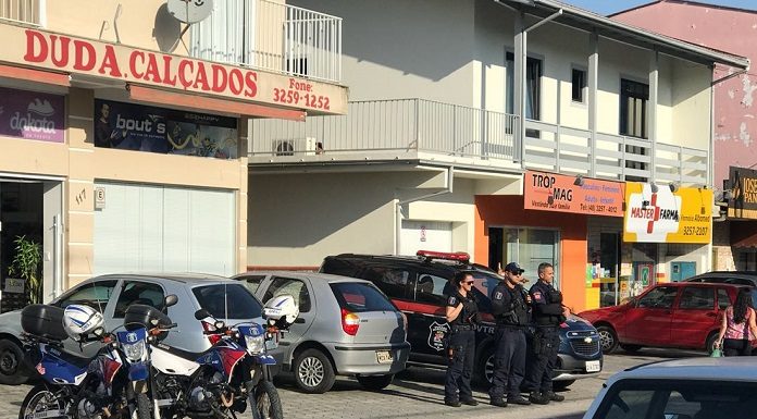 três agentes da guarda parados lado a lado na calçada em frente aos comércios observando o movimento da rua