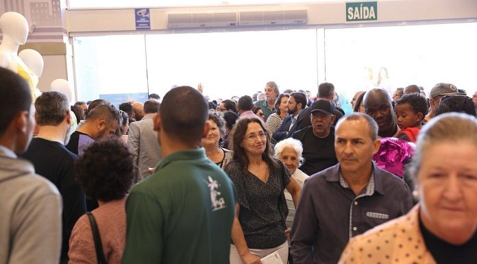 grande grupo de pessoas reunidas ocupa toda a imagem; é possível ver uma porta de vidro ao fundo