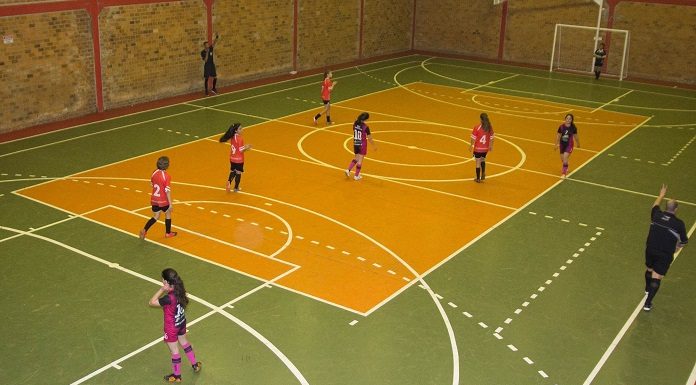 quadra de futsal onde estão jogando dois times de meninas