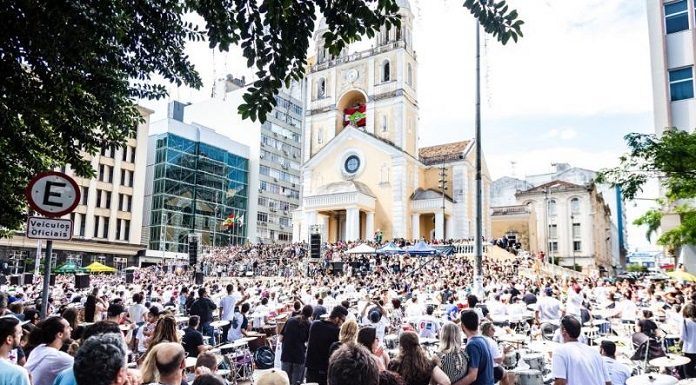 grande público em uma praã em frente a uma catedral assiste os vários bateristas