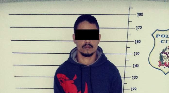 homem com o rosto censurado diante do quadro de medição de altura na delegacia posa para foto usando moletom