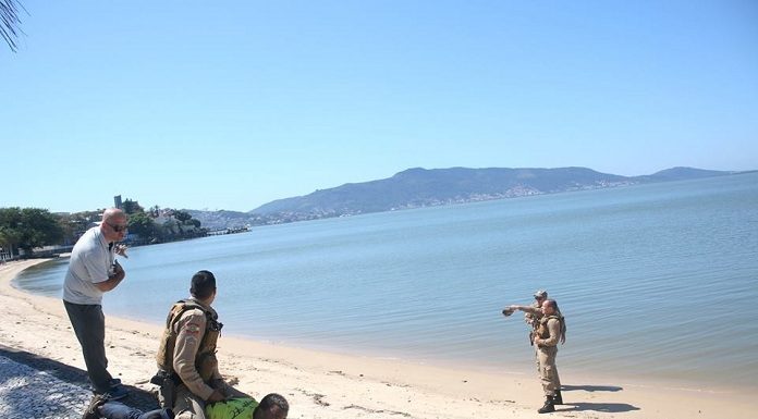 policial sentado em cima das costas do ladrão, que está deitado no chão da calçada; há uma praia ao lado, com dois policiais parados na areia apontando