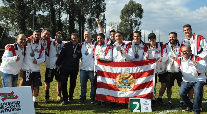 equipe posa para foto em gramado usando uniforme e bandeira de blumenau