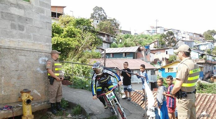 piloto faz uma curva de um caminho do morro observado por dois pm e um grupo de crianças ao lado