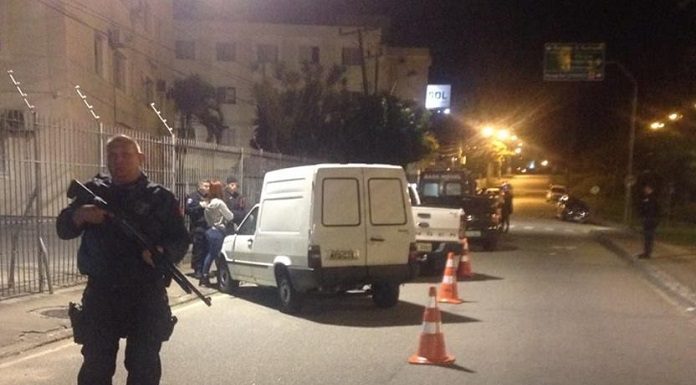 agente da gmsj segurando escopeta na frente de cones, com carros estacionando na blitz atrás e agentes circulando