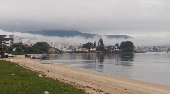 praia com mar calmo e enseada ao fundo com nevoeiro sobre o continente