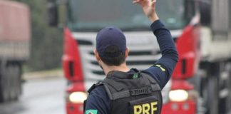 agente da prf visto de costas com uniforme da corporação gesticula com o braço direito para caminhão na estrada