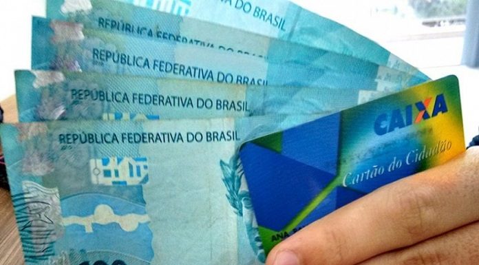 mão segura cartão cidadão e cinco cédulas de 100 reais