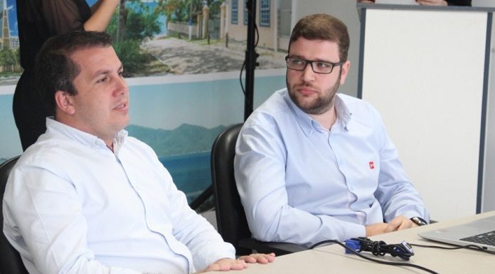 prefeito camilo fala sentado em frente a uma mesa, ao lado de outro homem de óculos que o observa