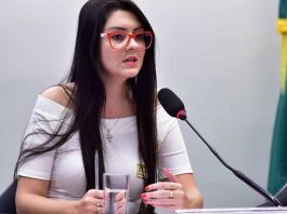 campagnolo fala em microfone sentada em frente a uma mesa