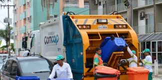 trabalhadores da comcap mexem em latões de lixo atrás de um caminhão de lixo, parado no meio de uma rua