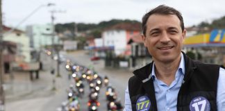 foto de moisés em cima de um caminhão, usando colete e adesivos do partido; há uma fila de motos que o acompanhando ao fundo na rua