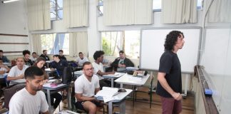 sala de aula com diversos homens sentado nas carteiras e professor olhando para o quadro